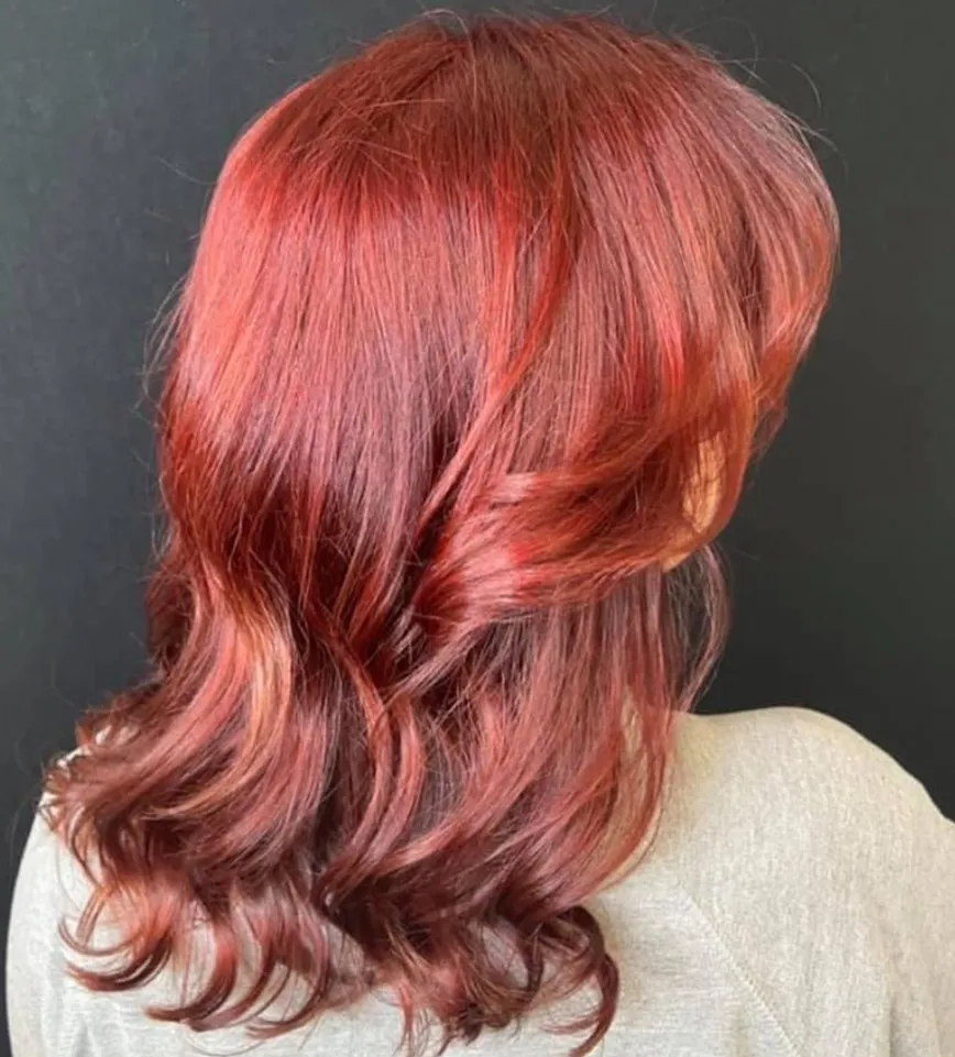 Person with shoulder-length, wavy, reddish-brown hair facing away from the camera, wearing a light gray top, against a plain black background—reflecting the serene atmosphere you might find during a deep tissue massage therapy session at a day spa in Covington, GA. - La Vie Spa & Salon in Covington, GA