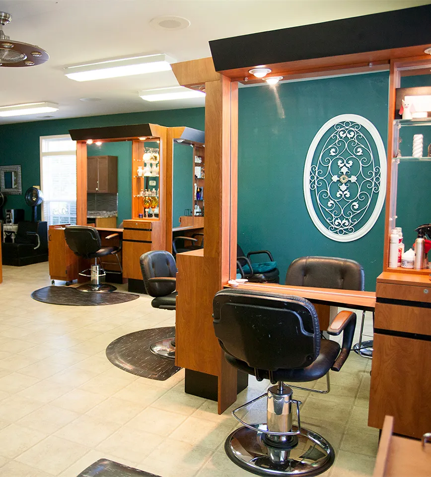 A modern salon interior at La Vie Spa & Salon features empty black chairs, wooden workstations, and teal walls complemented by a decorative white wall piece and various hair products on shelves. The serene ambiance invites guests to relax and enjoy the indulgent experience, whether booking Yon-Ka Paris facial treatments or deep tissue massage therapy. - La Vie Spa & Salon in Covington, GA
