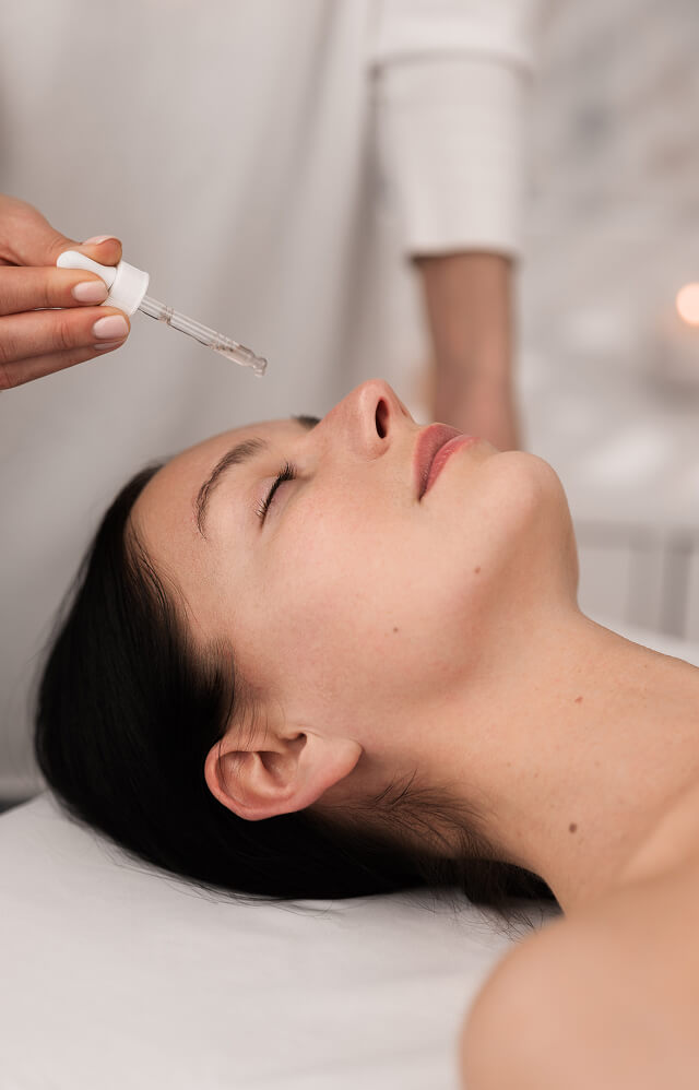 At La Vie Spa & Salon, a person lies peacefully on a spa bed with eyes closed while another hand holds a dropper, gently applying skincare serum to the face—a signature moment at this luxurious day spa in Covington, GA. - La Vie Spa & Salon in Covington, GA