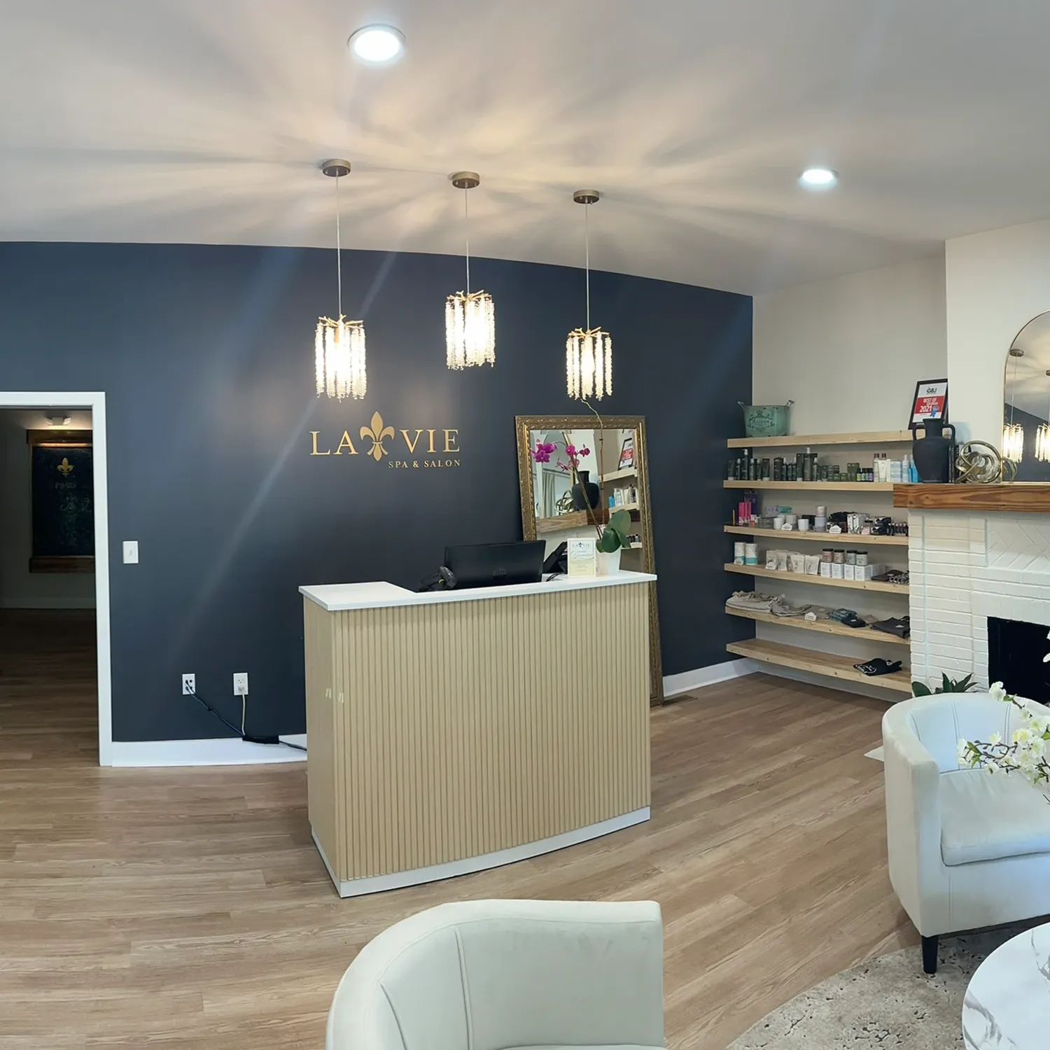 Reception area of a modern day spa in Covington, GA, with a wooden desk, pendant lights, product shelves featuring Yon-Ka Paris facial treatments, and a dark accent wall displaying the “La Vie Spa & Salon” logo. - La Vie Spa & Salon in Covington, GA